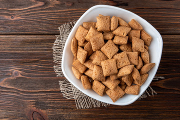 Dried breakfast pads in white bowl on dark wooden background.