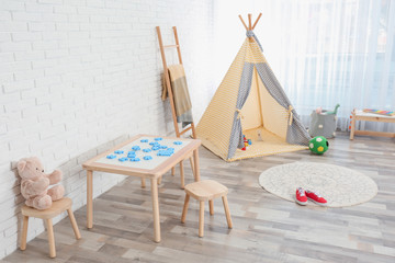 Fototapeta na wymiar Cozy kids room interior with table, stools and play tent
