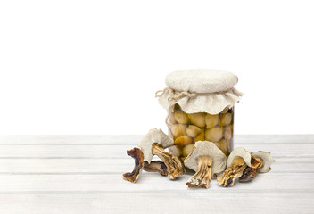 Dried mushroom Boletus edulis and marinated in glass jar on white wooden table on a white background