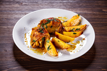 Grilled chicken thighs with baked potatoes on wooden table