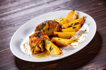 Grilled chicken thighs with baked potatoes on wooden table