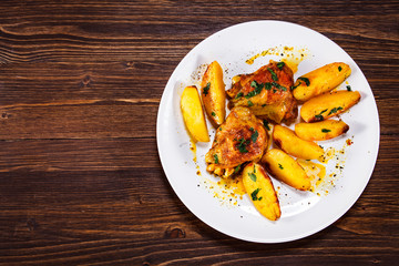 Grilled chicken thighs with baked potatoes on wooden table