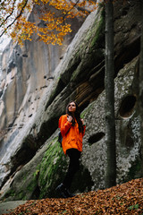 Young woman wearing warm orange sweater in the autumn forest. Misty landscape with mossy rocks. Cute smiley woman in the nature. Autumn forest hiking 