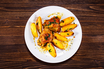 Grilled chicken thighs with baked potatoes on wooden table