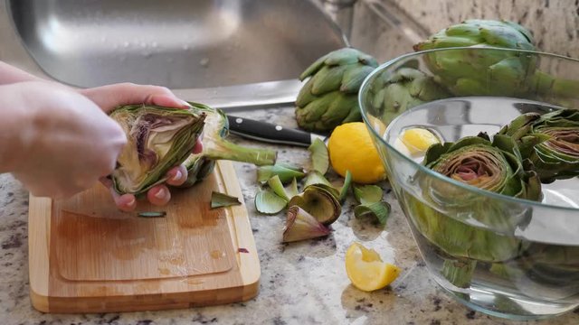 Woman cleaning heart of artichokes with spoon. Cooking process at modern kitchen