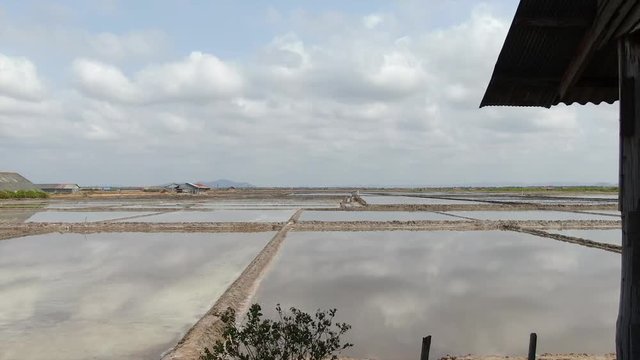 Low aerial view fly back from flooded salt farm brine field in Asia to reveal wooden storage shack on the frame right.