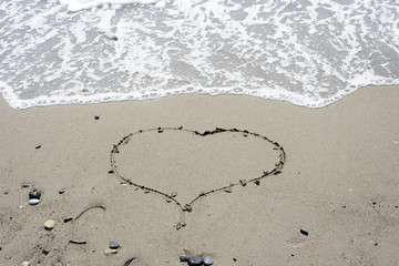 drawn on sand heart on the background of the sea waves