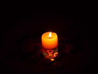 A lighted candle stands on the table. On the table are shiny colorful hearts.