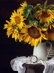 yellow sunflowers in a jug and a clock.
