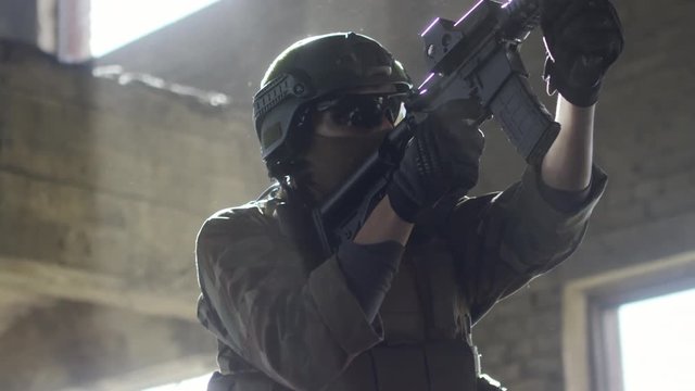Slow motion of armed soldier in balaclava and protective glasses walking with shotgun in abandoned building