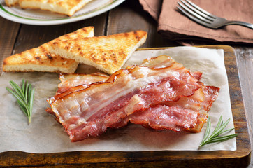 Fried bacon and toasts on cutting board