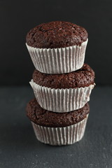 Chocolate homemade cupcakes muffins on a black background with chocolate drops in the background. Bakery style. Dark food photo vertical