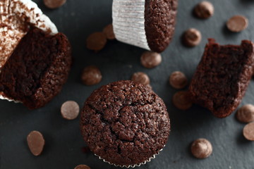 Chocolate homemade cupcakes muffins on a black background with chocolate drops in the background. Bakery style. Dark food photo