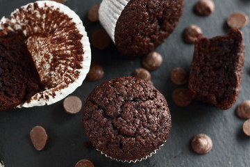 Chocolate homemade cupcakes muffins on a black background with chocolate drops in the background. Bakery style. Dark food photo