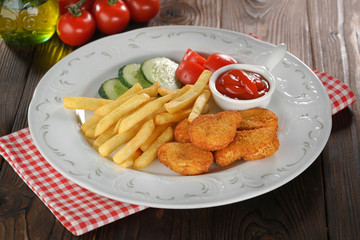 Chicken nuggets, french fries and vegetables in white plate on wooden table