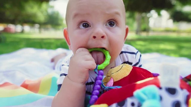 Cute baby boy with toy-rattle on colorful playmat in the park. Adorable child playing with a teething toy.