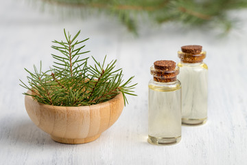 Pine essential oil in a glass bottle. Soft focus. White wooden background.