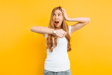 beautiful girl looking at a hand watch, points to the watch, on a yellow background, concept of being late