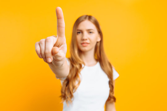 Woman touching an imaginary screen with her finger on a yellow background