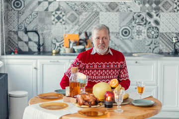 old bearded serious man in stylish clothes sitting at the table and looking aside. close up portrait.