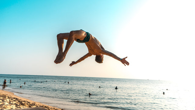 Sport beach.Backflip on the beach at sunset, gymnastic on the beautiful beach with acrobatic blanche ,young man doing sport exersices with motivation context