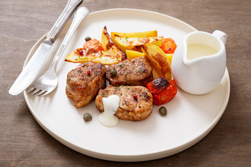 Pork meat medallions with baked potatoes and cream sauce .