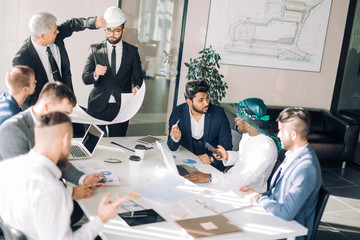 Interracial group of male architects and builders are engaged in lively discussion of the budget and building plan for a new object.