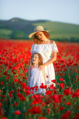 Mother and daughter in light dresses and hat walking on the farm field. Field of blooming poppies.