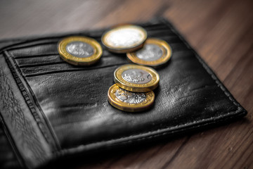 New Great British Pound GBP Coins laying casually on top of black wallet on wooden surface. Wealth, Money, Cash, Change.