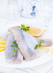 Marinated herring fillet on a white plate with lemon and onion. Traditional spring delicacy of the Netherlands. Typical cooking fish in Holland. Free space for text or brand.