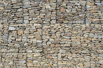 the wall of beautiful multi-colored stones covered with iron mesh