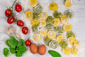 Homemade fresh Italian ravioli pasta on white wood table  with flour, basil, tomatoes,background,top view.