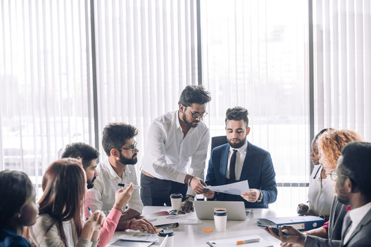 Relaxed informal IT business company meeting. Team leader in formal suit discussing new ways of vision and ideas of income increase with subordinates. Startup business and entrepreneurship concept