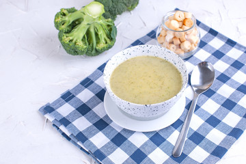 Cream soup puree with broccoli, cream and crackers. Lunch of vegetables on a light background. Plate and napkin on the table.