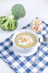 Cream soup puree with broccoli, cream and crackers. Lunch of vegetables on a light background. Plate and napkin on the table.