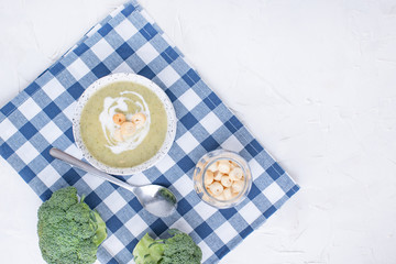 Cream soup puree with broccoli, cream and crackers. Lunch of vegetables on a light background. Plate and napkin on the table.