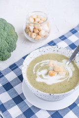 Cream soup puree with broccoli, cream and crackers. Lunch of vegetables on a light background. Plate and napkin on the table.