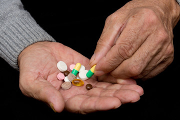 An elderly man holds a lot of colored pills in old hands. Painful old age. Health care of older...