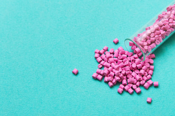 Plastic pellets. Pink Plastic granules from the tube on a turquoise background. Plastic Raw...