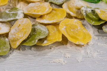 Homemade fresh Italian ravioli pasta on white wood table  with flour close-up.
