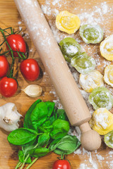 Homemade fresh Italian ravioli pasta on wood table  with flour, basil,tomatoes,background,top view.