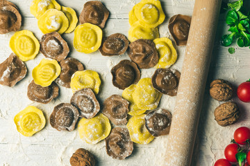 Homemade fresh Italian ravioli pasta on white wood table  with flour, basil, tomatoes,background,top view.