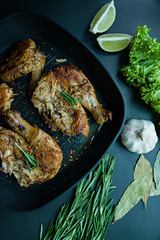 Grilled chicken in a grill pan, decorated with spices for meat, rosemary, vegetables on a dark background. View from above