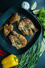 Grilled chicken in a grill pan, decorated with spices for meat, rosemary, vegetables on a dark background. View from above