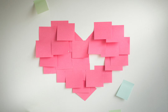Blank pink sticky notes sticked in a heart shape on wall. 
