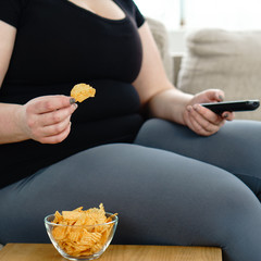 overeating, sedentary lifestyle, bad habits, food addiction, eating disorders. fat overweight woman lay on the coach with tv remote and junk food. depression, laziness