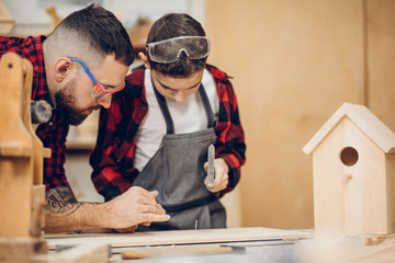 Carpenter building a wooden nesting box together with his kid. A little son is participating...