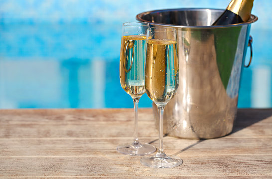 Champagne glasses and bottle in ice bucket near swimming pool