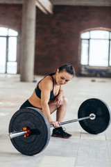 Fototapeta na wymiar full length side view photo of a slim girl sitting near the barbell. relaxation,pensive female athlete looking at the barbell and preparing to lift it