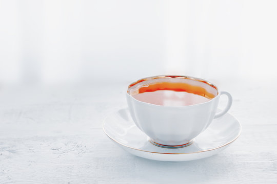 Tea in white cup on white table. Hot morning tea drink background with copy space. High key image of cup of tea